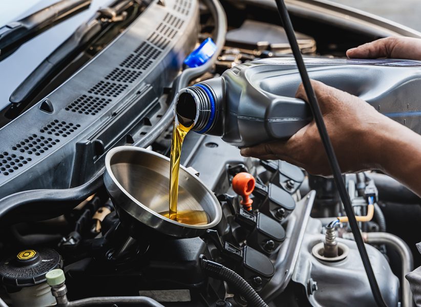 Car mechanic pouring engine oil into vehicle during doing car maintenance in garage